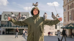 man in green jacket with pigeons on him