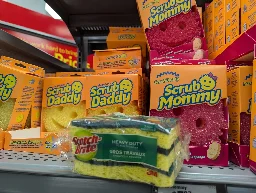a shelf with Scrub Daddies on the left, Scrub Mommies on the right, with a small pack of scotch brite scrubbers in the middle