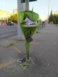 a melted trash can with a cigarette bin barely holding onto it
