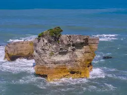 A rock outcropping in the middle of ocean waves.  The outcropping shows many thin layers, suggestive of a stack of pancakes layered one on top of the other